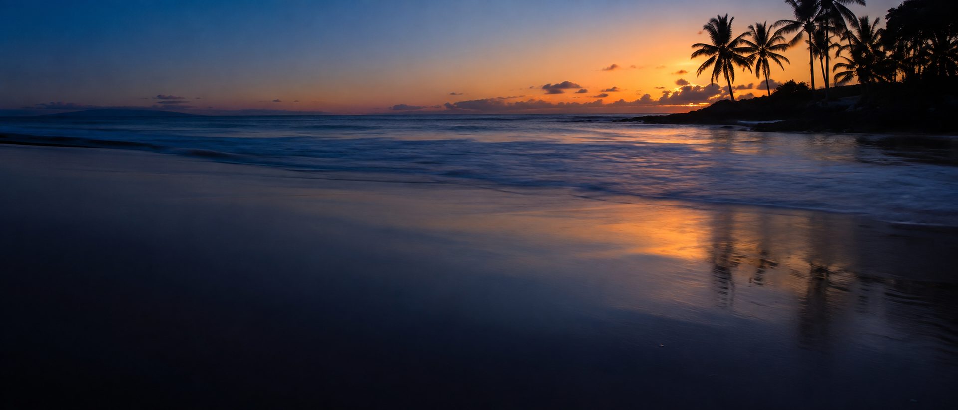 A quiet tropical shoreline at dusk, palms against an orange sky
