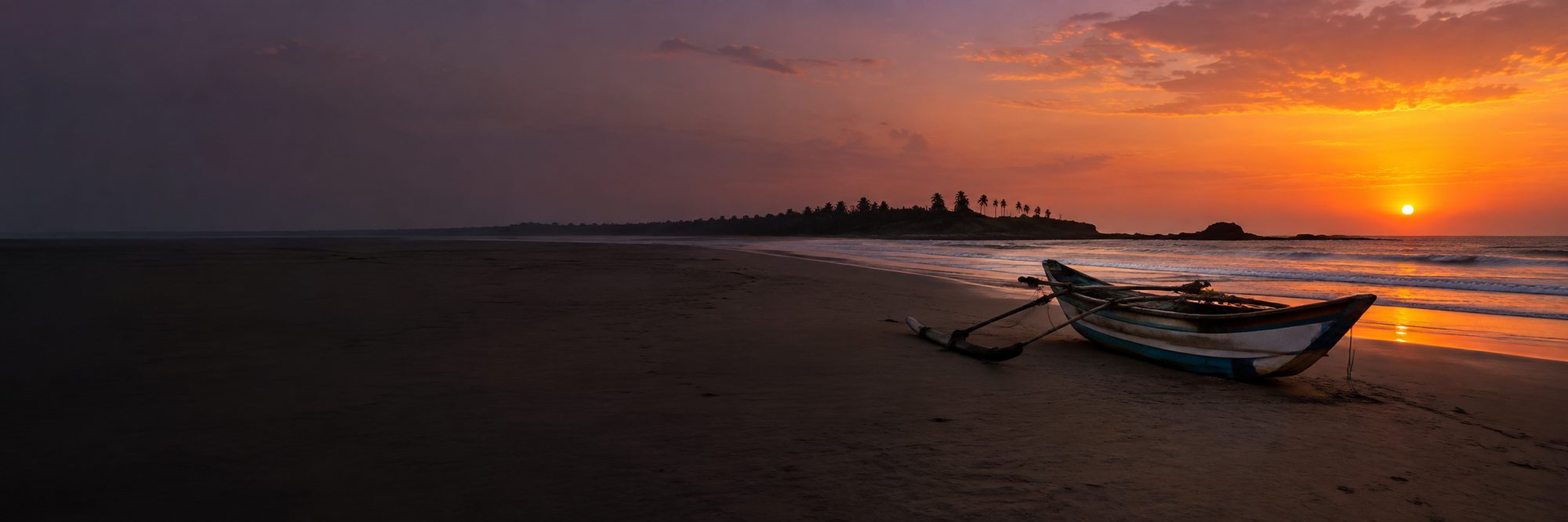 An outrigger fishing boat on an empty Sri Lankan beach at sunset