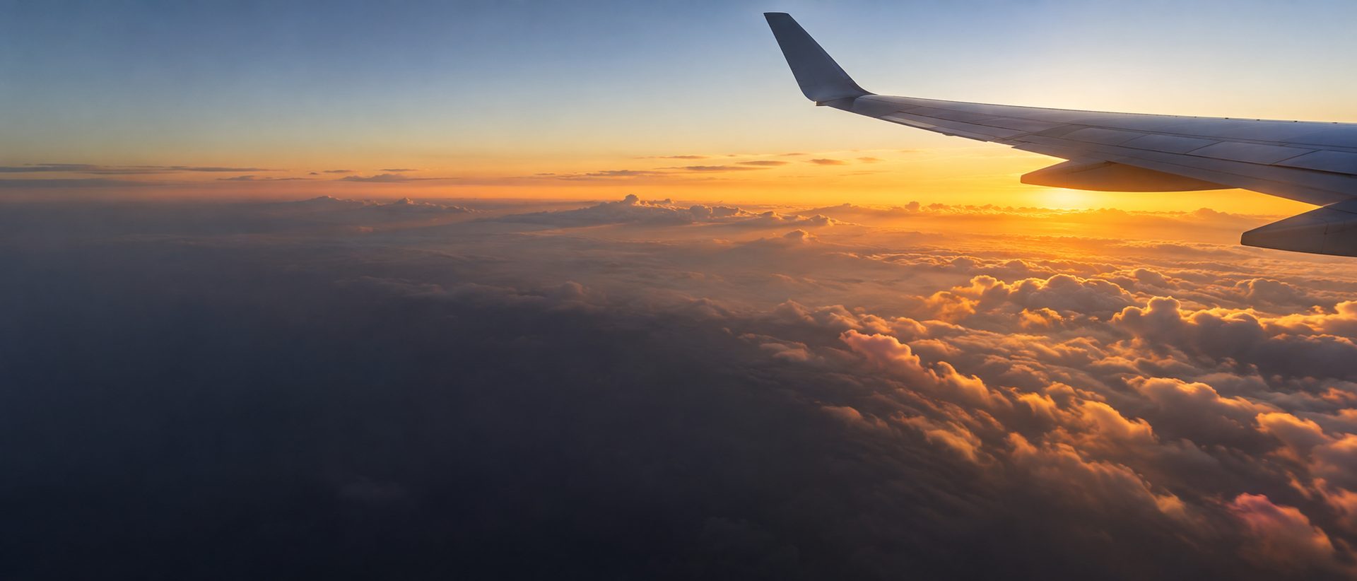 An aircraft wing above golden clouds at sunset